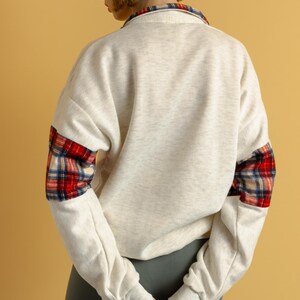 May include: A cream-colored sweatshirt with red and black plaid fabric on the sleeves. The sweatshirt has a relaxed fit and a crew neck.