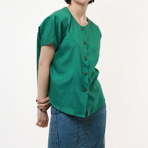 Puede incluir: Una mujer con una camisa verde de botones con mangas cortas y una falda vaquera.