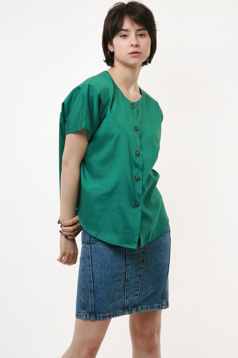 Puede incluir: Una mujer con una camisa verde de botones con mangas cortas y una falda vaquera.