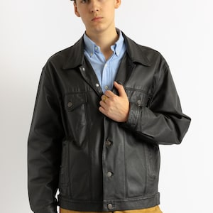 May include: A black leather jacket with a button-up front and a light blue button-down shirt underneath.