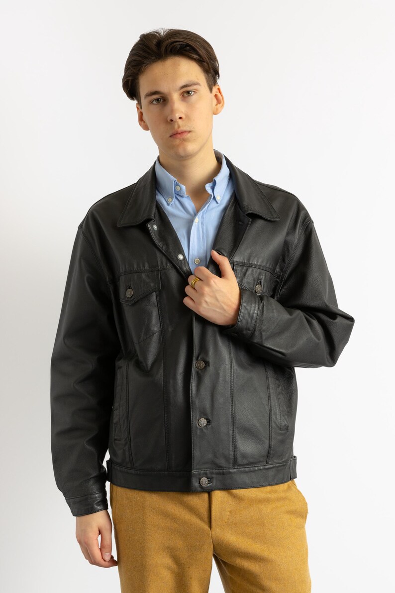 May include: A black leather jacket with a button-up front and a light blue button-down shirt underneath.