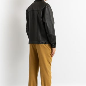 May include: A black leather jacket with a button closure and a brown pair of pants.