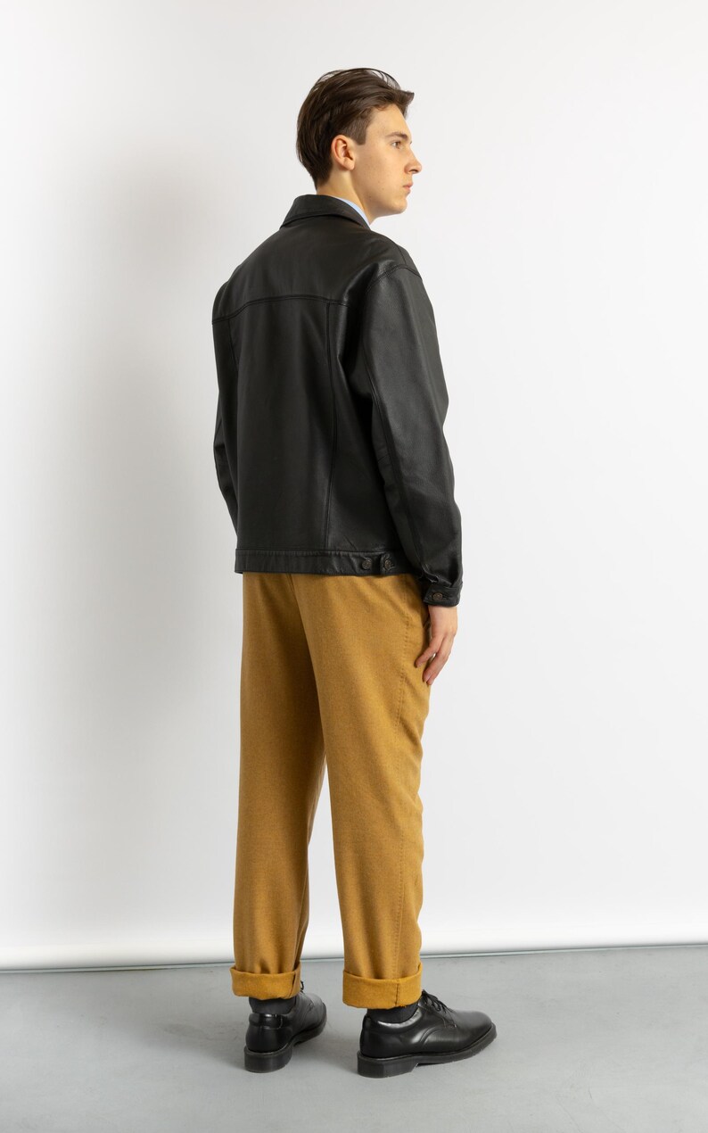 May include: A black leather jacket with a button closure and a brown pair of pants.