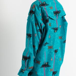 May include: A turquoise blue long-sleeved shirt with a colorful geometric pattern. The shirt has a pointed collar and a button-up front.