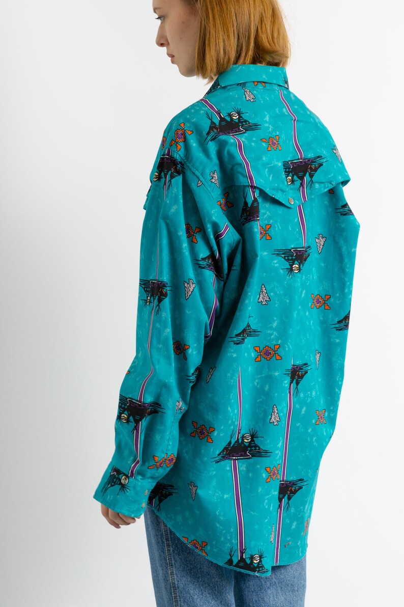 May include: A turquoise blue long-sleeved shirt with a colorful geometric pattern. The shirt has a pointed collar and a button-up front.