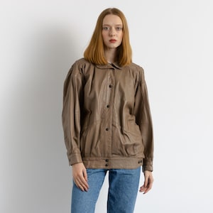 May include: A brown leather jacket with a button-up front and long sleeves. The jacket has a relaxed fit and a slightly oversized look.