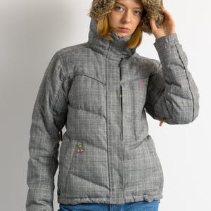 Puede incluir: Una chaqueta de invierno gris a cuadros con capucha forrada de piel sint&eacute;tica. La chaqueta tiene un dise&ntilde;o acolchado y un cuello alto. Cuenta con cierre de cremallera y bolsillos. El modelo lleva vaqueros azules.