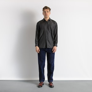 以下が含まれることがあります： ダークグレーのボタンダウンシャツとネイビーブルーのコーデュロイパンツを着た人。 シャツは長袖で、クラシックな襟が付いています。 パンツはストレートレッグです。 その人は茶色の革靴を履いています。