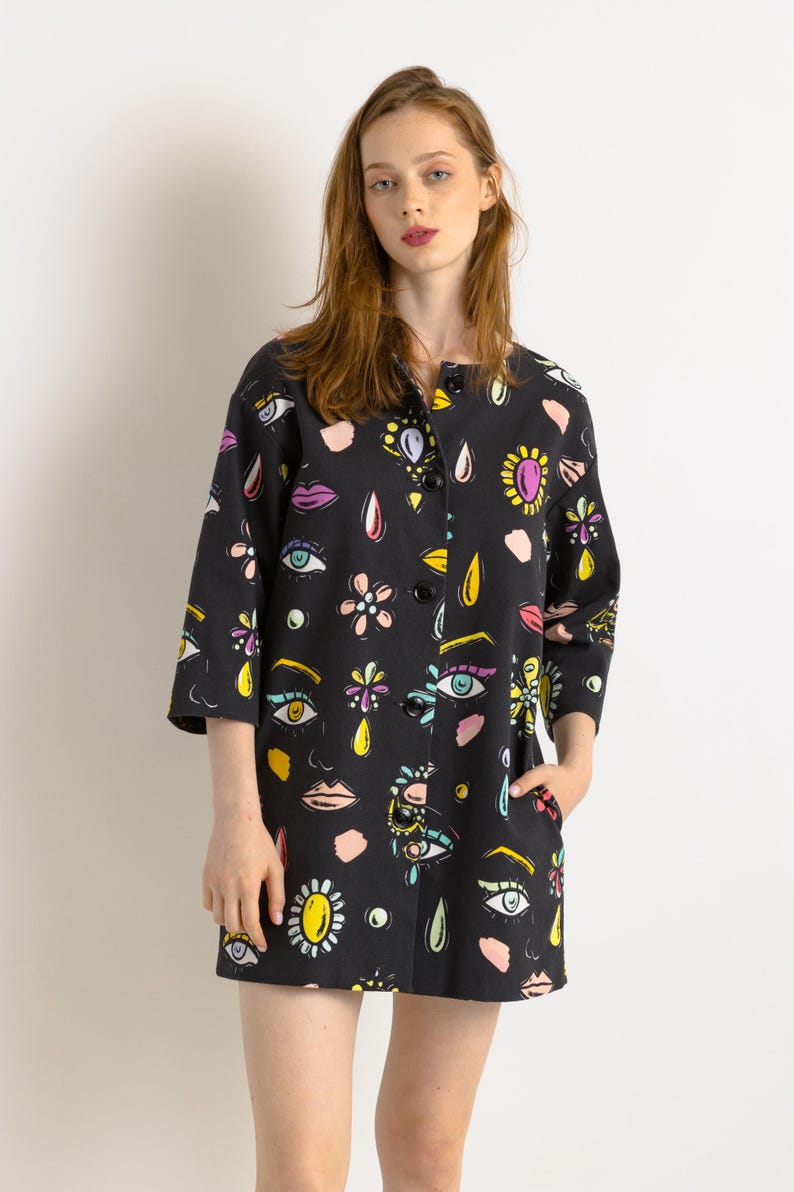 May include: A black button-up jacket with a colorful print of eyes, lips, flowers, and teardrop shapes. The jacket has a collar and three-quarter sleeves.