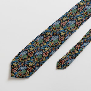 Pode incluir: Uma gravata azul escura com um padrão floral colorido com pássaros e flores. A gravata tem uma largura estreita e uma ponta pontiaguda.