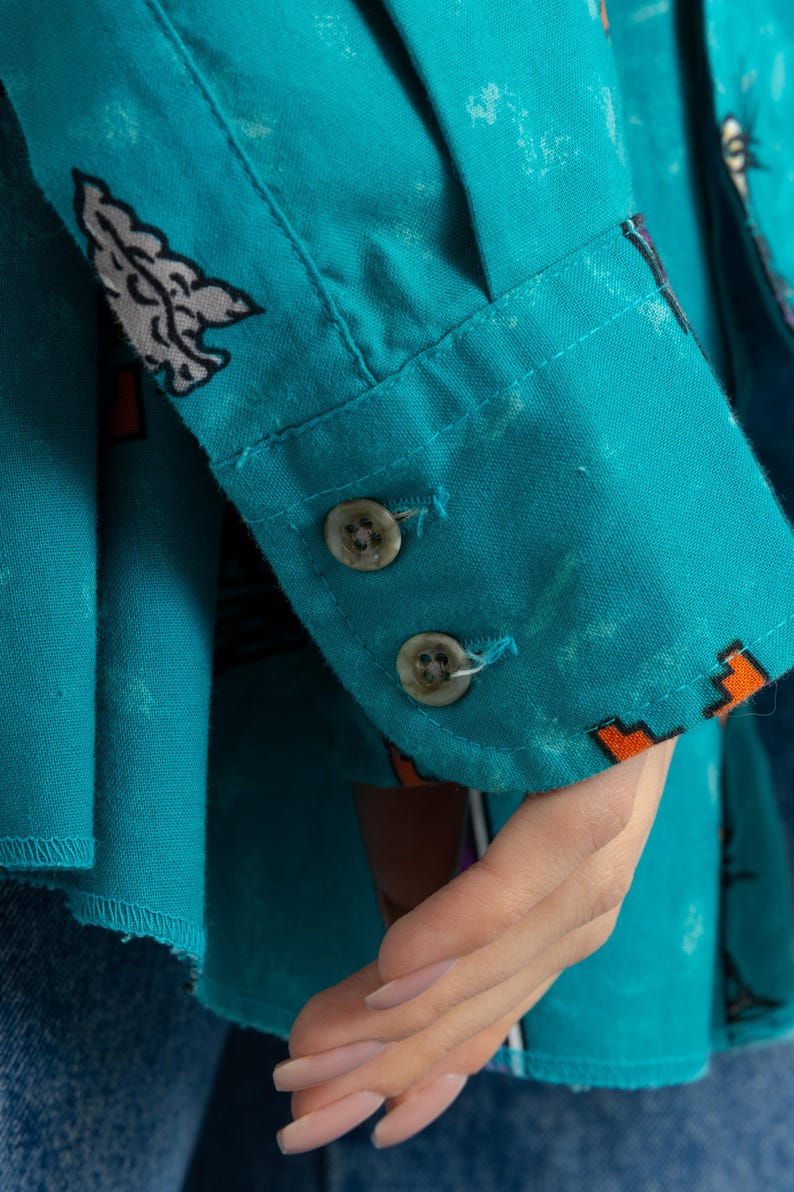 May include: A turquoise blue button-down shirt with a colorful abstract print. The shirt has two white buttons on the cuff.