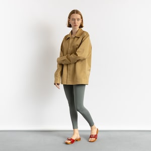 May include: A woman wearing a brown oversized shirt and gray leggings. She is wearing red sandals with a buckle.