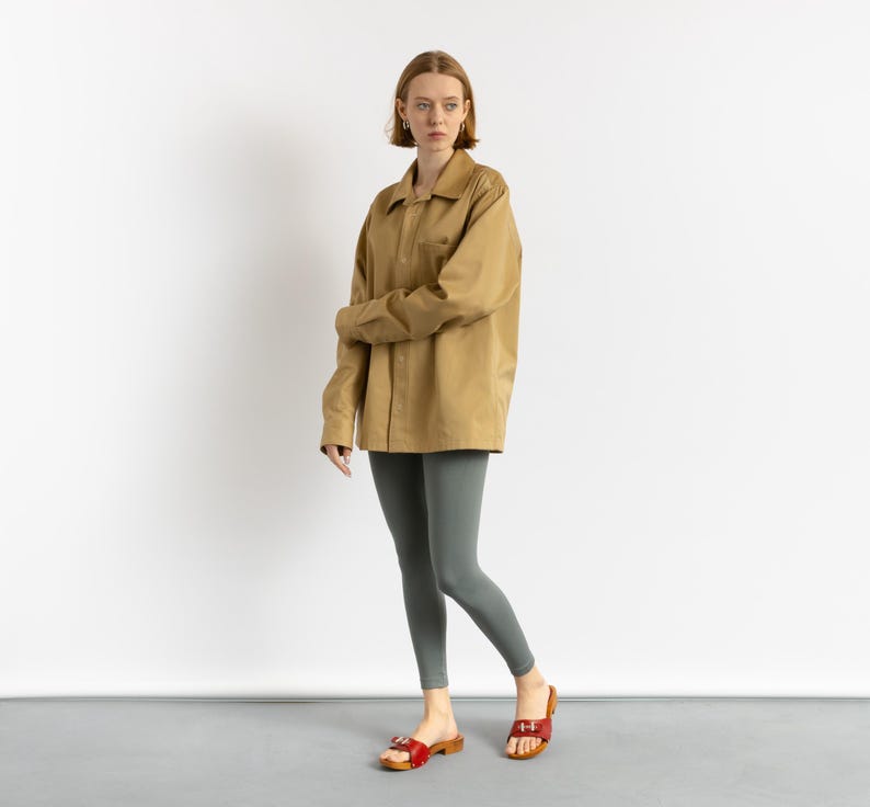 May include: A woman wearing a brown oversized shirt and gray leggings. She is wearing red sandals with a buckle.