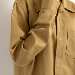 May include: A long-sleeved, tan button-down shirt with a single chest pocket and a relaxed fit.