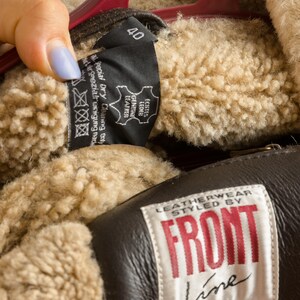 May include: Close-up of a brown leather jacket with a beige shearling lining. The jacket has a label that reads "LEATHERWEAR STYLED BY FRONT Line". A tag shows size 40 and "GENUINE LEATHER".