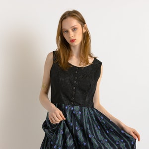Könnte beinhalten: Eine Frau trägt ein schwarzes, ärmelloses Kleid mit einem Rock mit Blumenmuster. Das Kleid hat einen Knopfleisten vorne und ein tailliertes Oberteil.