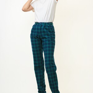 May include: A woman wearing a white t-shirt and green and blue plaid pants. She is wearing black heels.
