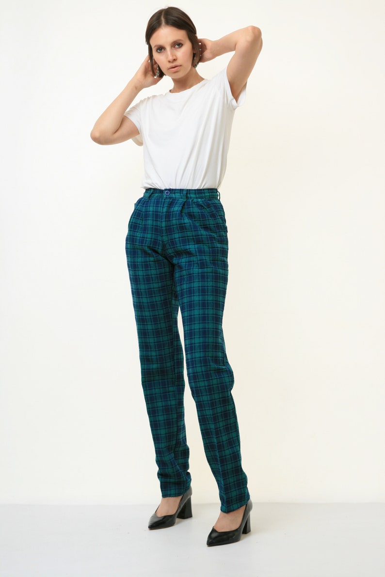 May include: A woman wearing a white t-shirt and green and blue plaid pants. She is wearing black heels.