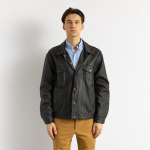 May include: A black leather jacket with a blue button-down shirt underneath. The jacket has a classic design with a collar, button closure, and two pockets.