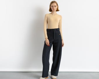 May include: A woman wearing a light beige long-sleeved shirt and dark blue wide-leg pants.