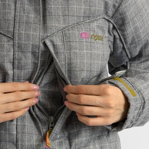 Puede incluir: Chaqueta gris a cuadros con cierre de cremallera y un peque&ntilde;o logotipo rosa y verde en el pecho. La chaqueta tiene capucha y un acento amarillo en la manga. El tirador de la cremallera tiene un dise&ntilde;o colorido.