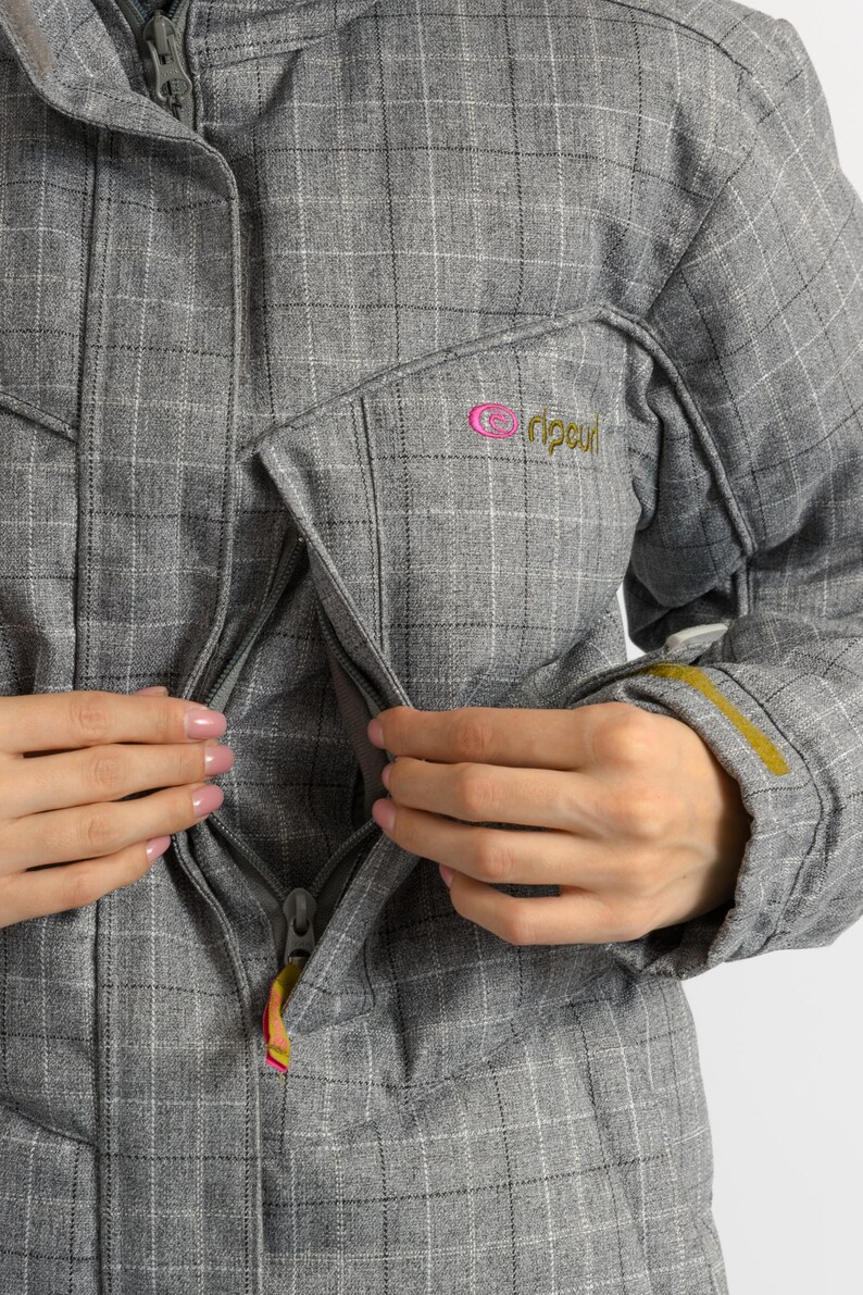 Puede incluir: Chaqueta gris a cuadros con cierre de cremallera y un peque&ntilde;o logotipo rosa y verde en el pecho. La chaqueta tiene capucha y un acento amarillo en la manga. El tirador de la cremallera tiene un dise&ntilde;o colorido.