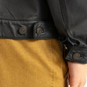 May include: Black leather jacket with a brown fleece lining. The jacket has a button closure and two pockets on the front. The jacket is shown with a brown corduroy shirt underneath.