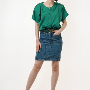 Puede incluir: Una mujer con una camisa verde de botones con mangas cortas y una falda vaquera. Lleva un cintur&oacute;n verde y tacones negros.