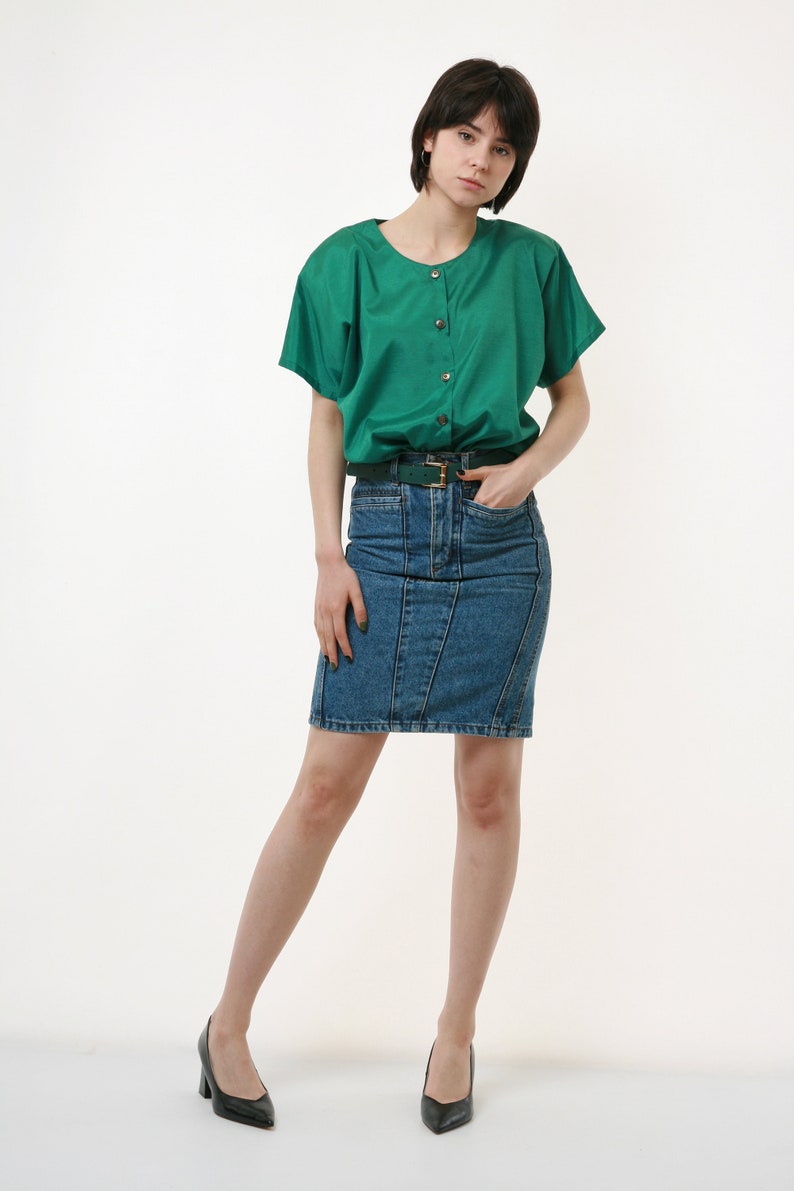 Puede incluir: Una mujer con una camisa verde de botones con mangas cortas y una falda vaquera. Lleva un cintur&oacute;n verde y tacones negros.