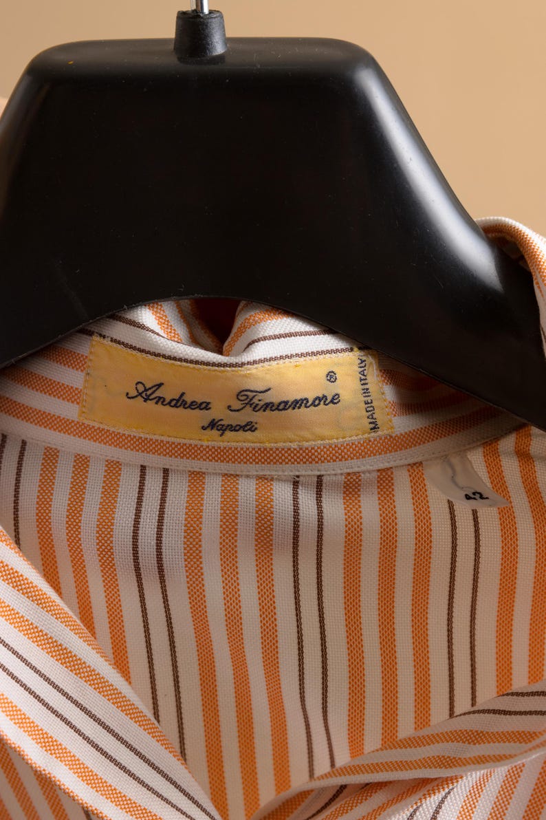Puede incluir: Una camisa de vestir a rayas naranja y blanca con una raya marr&oacute;n. La camisa tiene una etiqueta que dice "Andrea Finamore Napoli" y "Made in Italy".