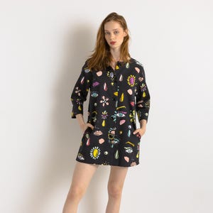 May include: A black button-down shirt with a colorful eye and lip print. The shirt has a relaxed fit and three-quarter sleeves.