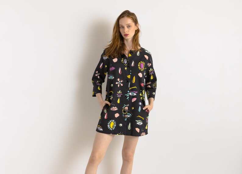 May include: A black button-down shirt with a colorful eye and lip print. The shirt has a relaxed fit and three-quarter sleeves.