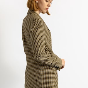 May include: A houndstooth blazer in black and tan. The tailored jacket features a classic pattern, notched lapels, and buttoned cuffs. The blazer is worn with blue jeans.
