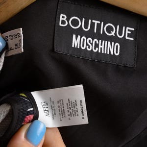 May include: Black Boutique Moschino label with white text. A white tag with black text indicates the fabric composition: 97% cotton, 3% other fibers. The tag also includes the size information: 40, GB 12, USA 10. The tag number is R A06021150.