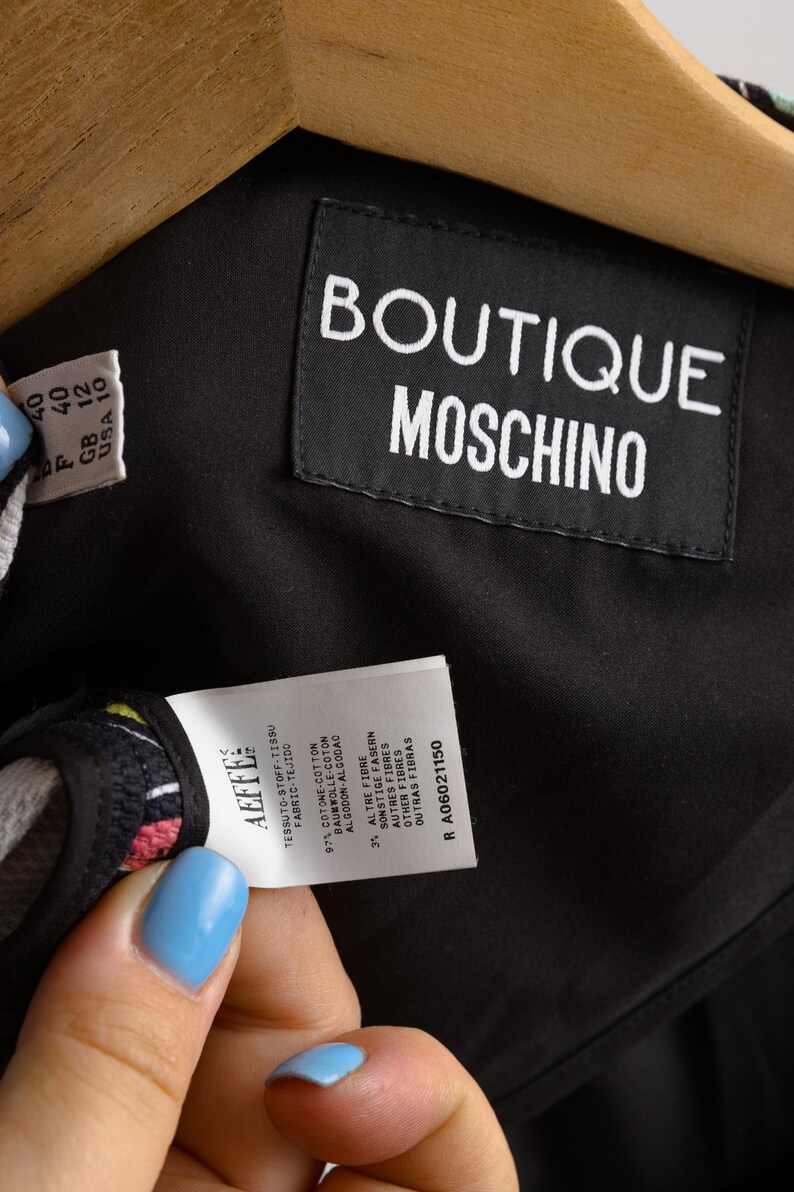 May include: Black Boutique Moschino label with white text. A white tag with black text indicates the fabric composition: 97% cotton, 3% other fibers. The tag also includes the size information: 40, GB 12, USA 10. The tag number is R A06021150.