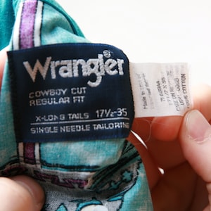 May include: A blue and white Wrangler brand cowboy cut, regular fit, long tail shirt with single needle tailoring. The tag says "X-Long Tails 17 1/2 - 35".