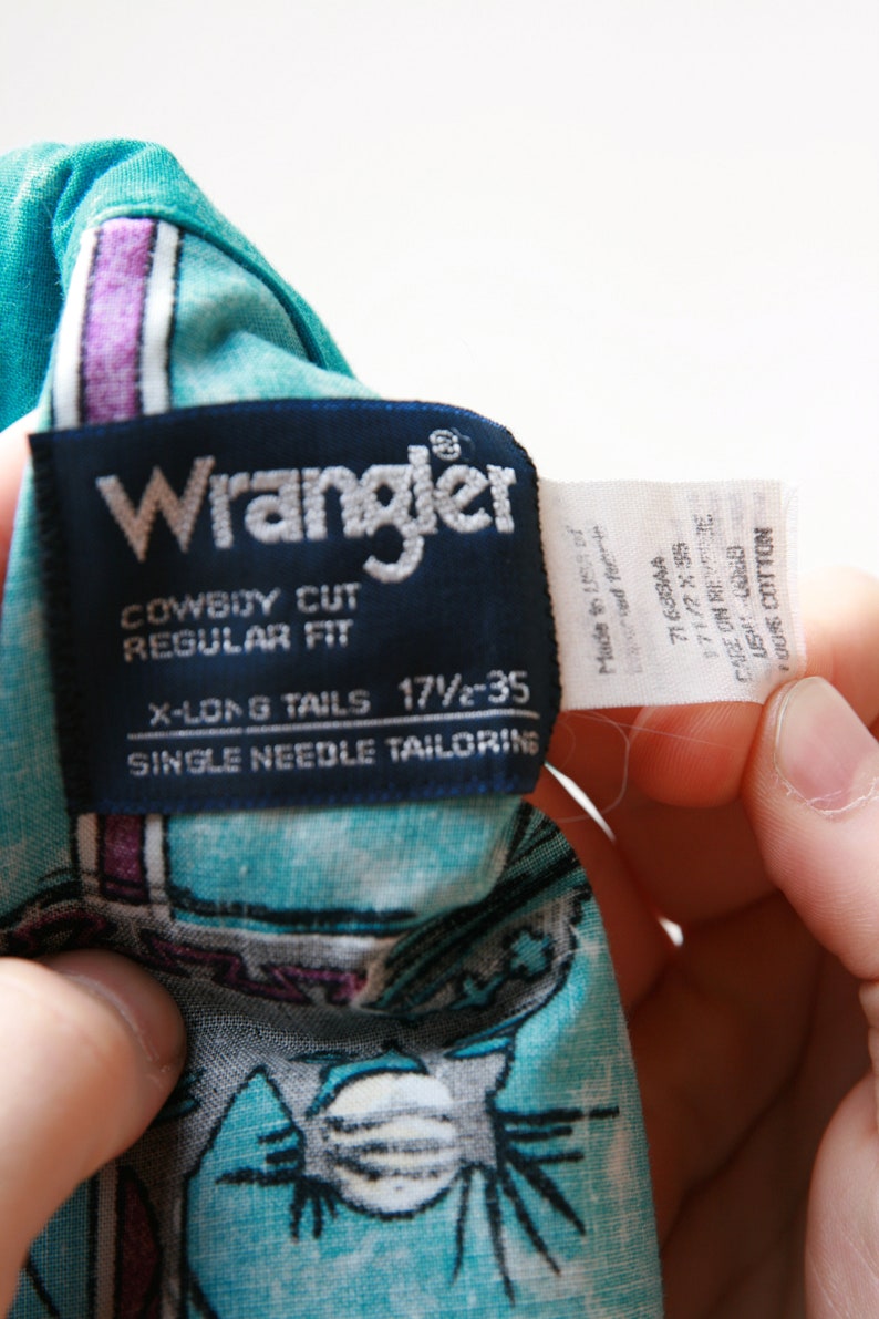 May include: A blue and white Wrangler brand cowboy cut, regular fit, long tail shirt with single needle tailoring. The tag says "X-Long Tails 17 1/2 - 35".