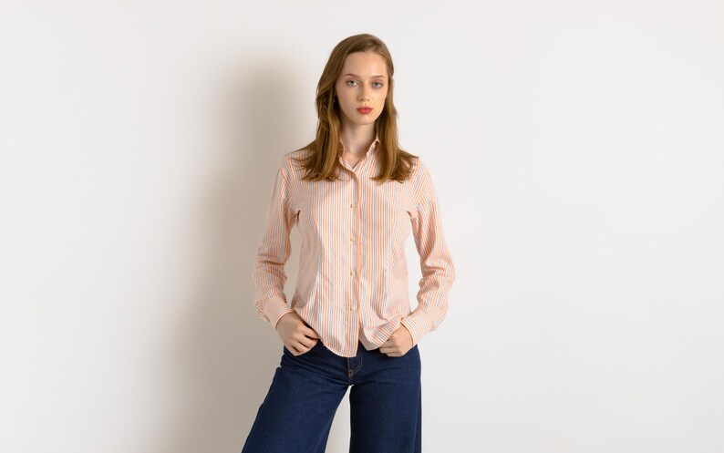 Puede incluir: Una mujer con una camisa de manga larga a rayas rosa y blanca y pantalones vaqueros azules.