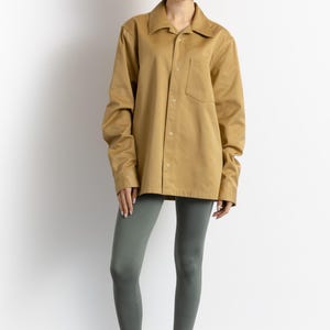 May include: A woman wearing a khaki button-down shirt with a chest pocket, gray leggings, and red wooden clogs.