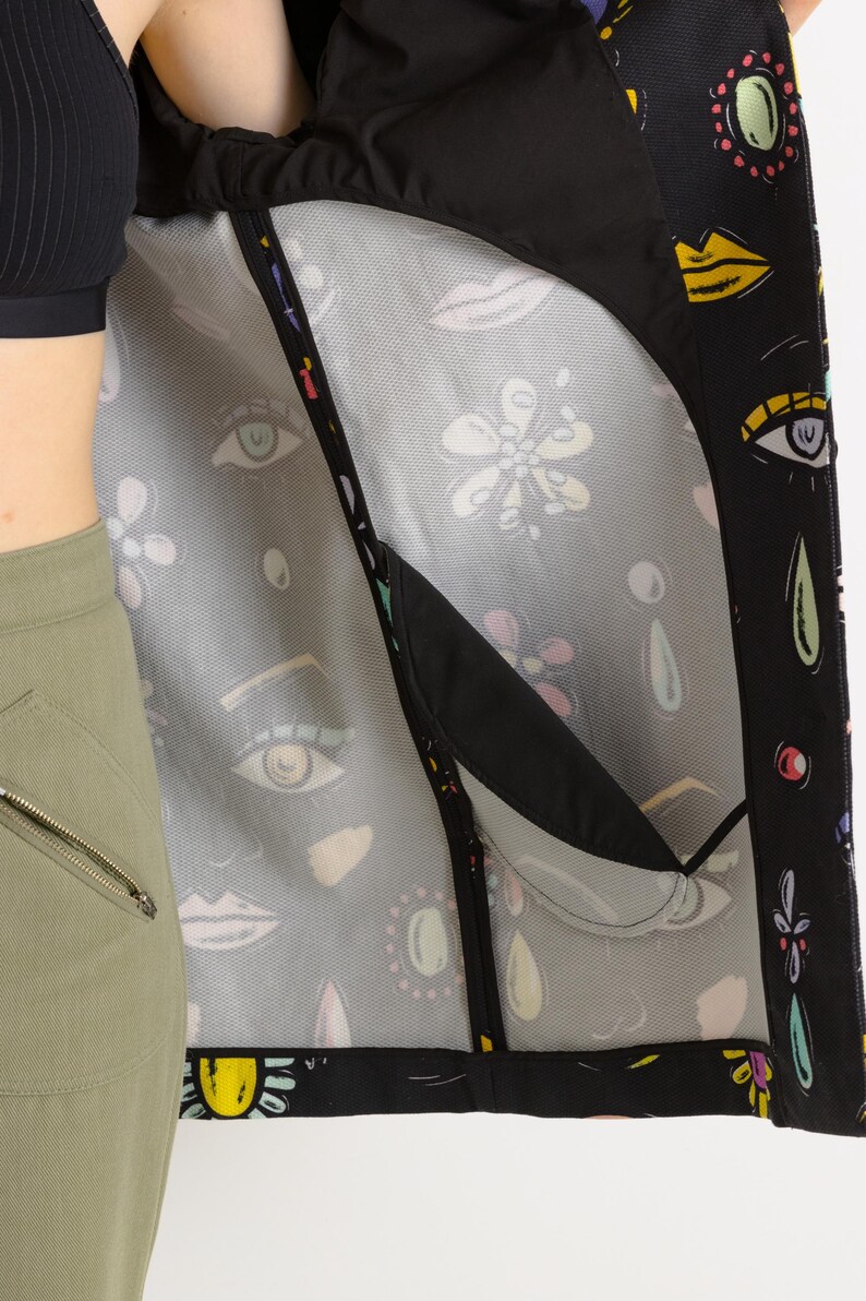 May include: A black jacket with a colorful, abstract print featuring eyes, lips, and flowers. The jacket has a mesh lining and a zipper closure.