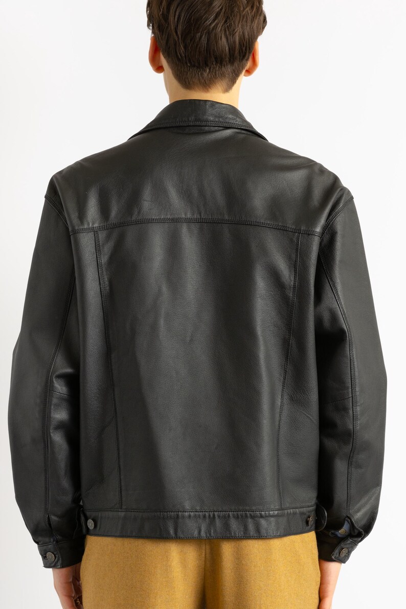 May include: A black leather jacket with a button-up front and a collar. The jacket has a classic denim jacket style.