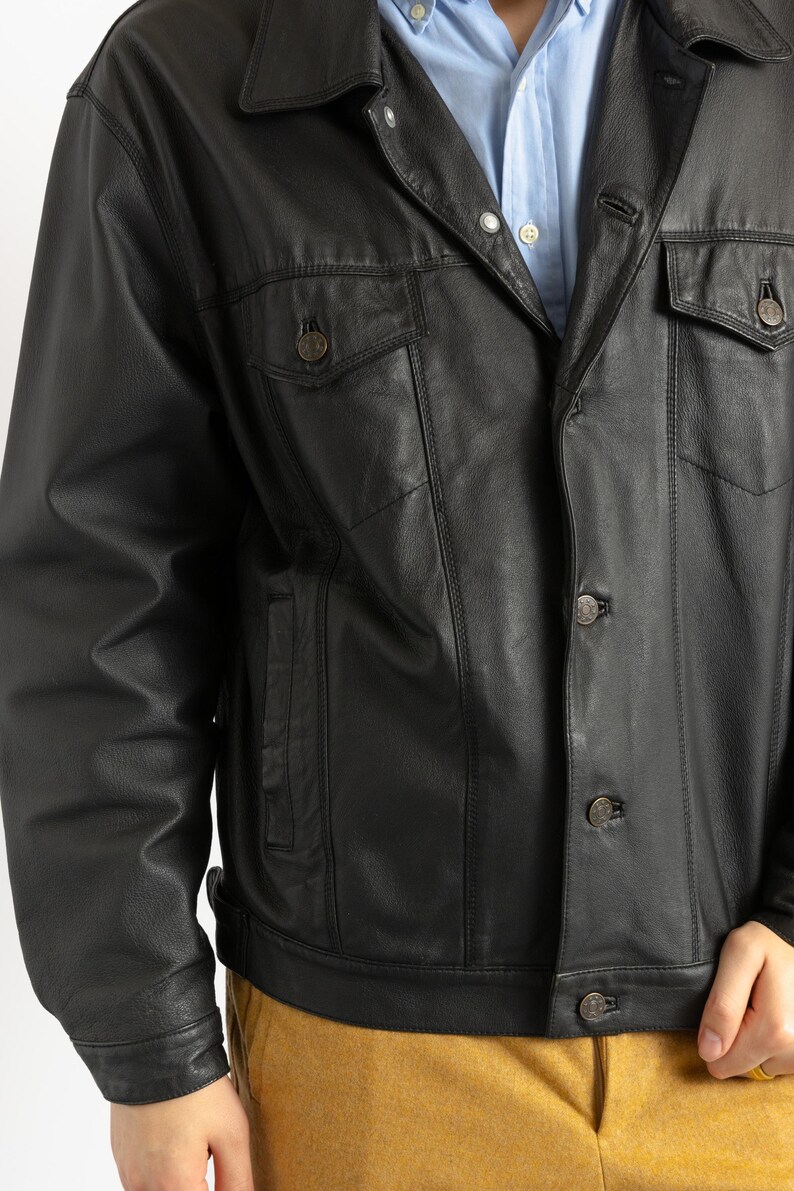 May include: A black leather jacket with a button-up front and a classic denim jacket style. The jacket has two flap pockets on the chest and two side pockets.