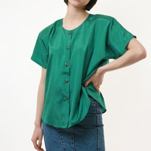 Puede incluir: Una mujer con una camisa verde de botones con mangas cortas y una falda vaquera.