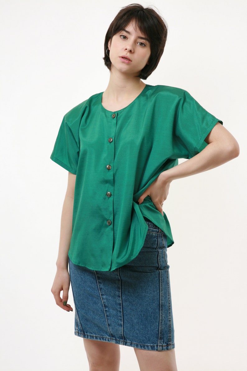 Puede incluir: Una mujer con una camisa verde de botones con mangas cortas y una falda vaquera.