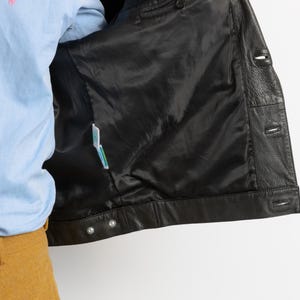 May include: Black leather jacket with a snap closure and a buttoned front. The jacket is unzipped and turned inside out, revealing a black lining.
