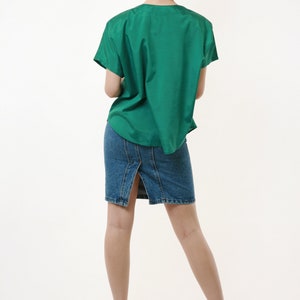 Puede incluir: Una mujer con una camisa verde de manga corta y una falda vaquera con una abertura en la espalda. Lleva tacones negros.
