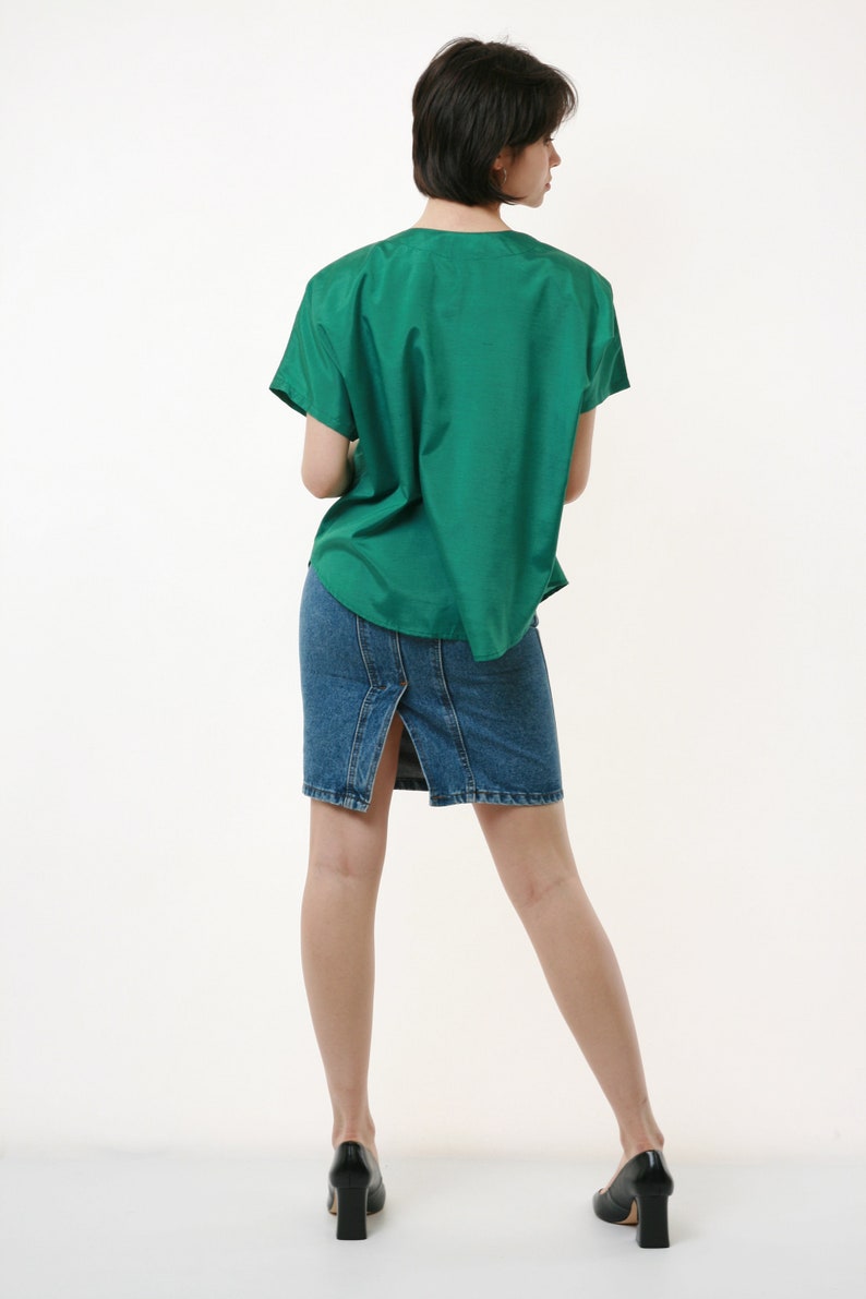 Puede incluir: Una mujer con una camisa verde de manga corta y una falda vaquera con una abertura en la espalda. Lleva tacones negros.