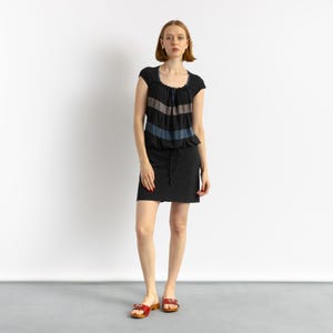 May include: A woman wearing a black and grey striped dress with a black skirt and red sandals.