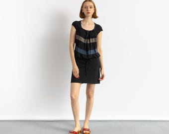 Könnte beinhalten: Eine Frau trägt ein schwarz-graues gestreiftes Kleid mit schwarzem Rock und roten Sandalen.