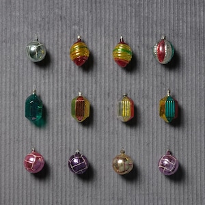 May include: A collection of vintage Christmas ornaments in various shapes and colors. The ornaments include silver, red, green, gold, and purple hues. Some have ribbed or faceted designs, while others are spherical or teardrop-shaped.